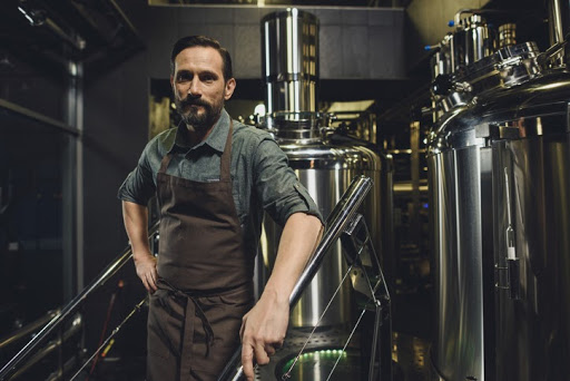 The owner if a craft brewery stands in front of some machinery. COVIDTRA includes tax provisions that could provide savings for craft breweries.