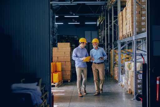Manufacturing merger and acquisition hesitancy over the past few years has caused pent up demand. Two professionals in hardhats touring a manufacturing facility.