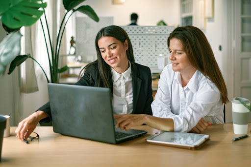 Two women looking at a laptop discussing the tax law governing exempt organization executive compensation.