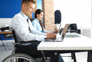 The Work Opportunity Tax Credit (WOTC) can provide significant tax savings to employers who recruit new employees from the credit’s qualified groups. Disabled veteran and a female colleague at a desk working on laptops.