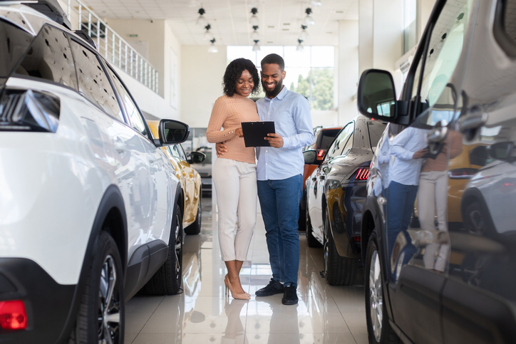 A couple looking at cars at a dealership showroom discusses how the Inflation Reduction Act might impact their purchase.