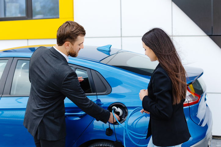 A woman is purchasing a blue electric vehicle from a salesman. Buyers like this one may be eligible for electric vehicle tax credits in 2024.