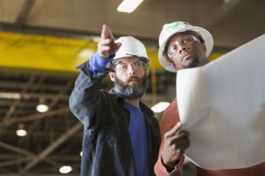 Two workers wearing hardhats with plans.web